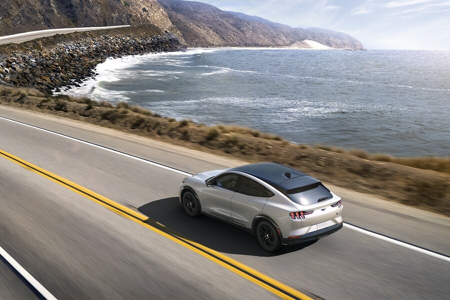Un Ford Mustang Mach E en argent roule sur une route côtière